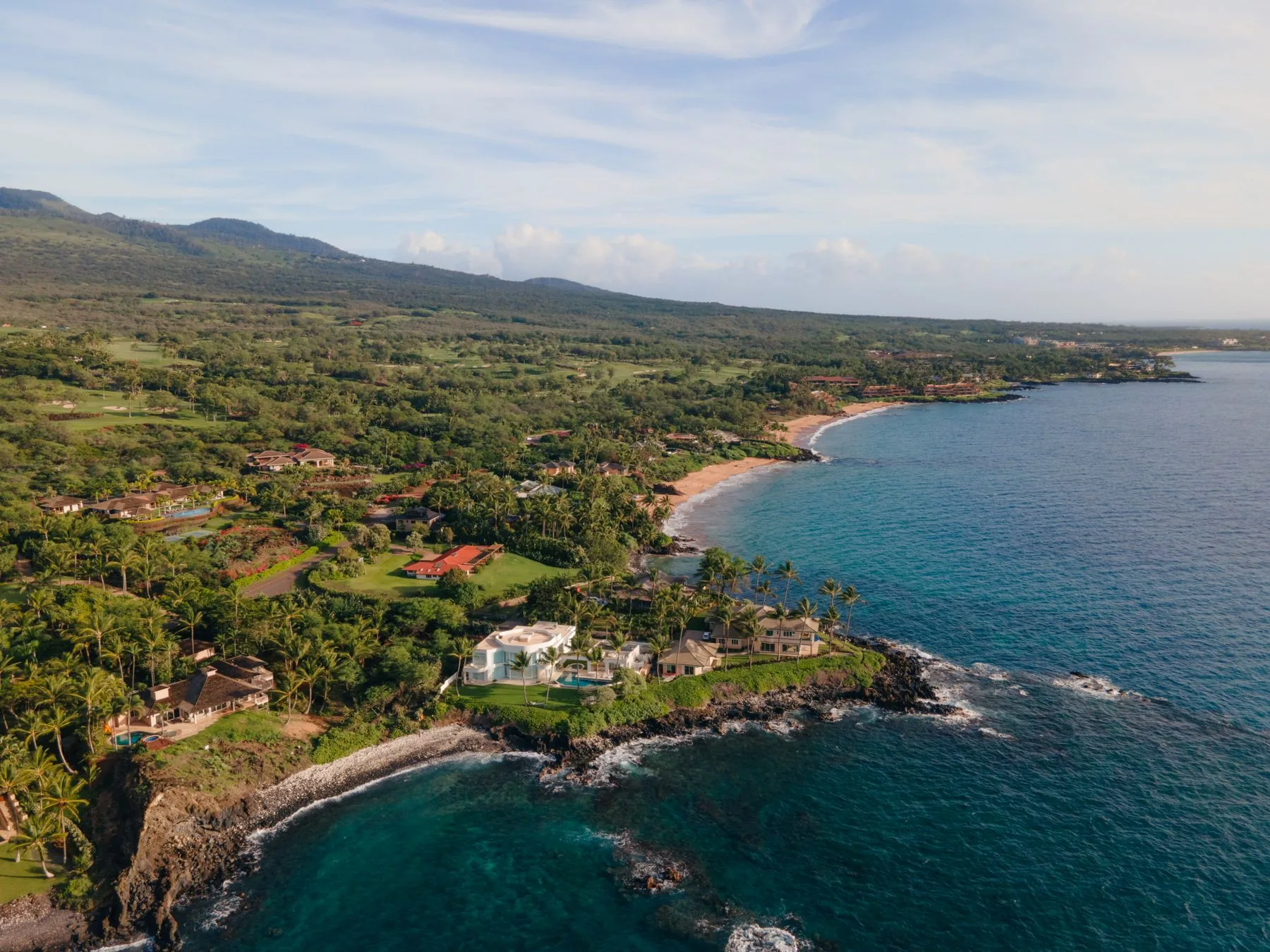 Aerial daylight view of a luxury South Maui coastline, homes and turquoise water below the mountains